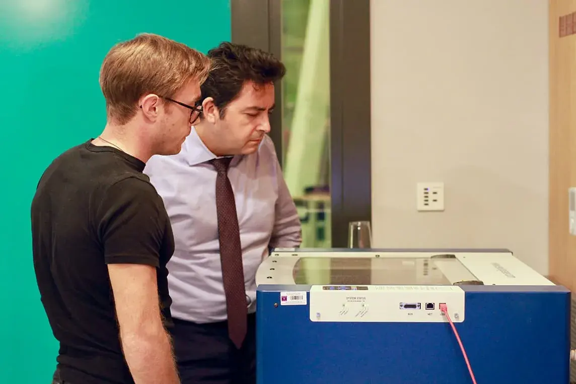 Two participants working at a laser cutter in the Al Warsha workshop.